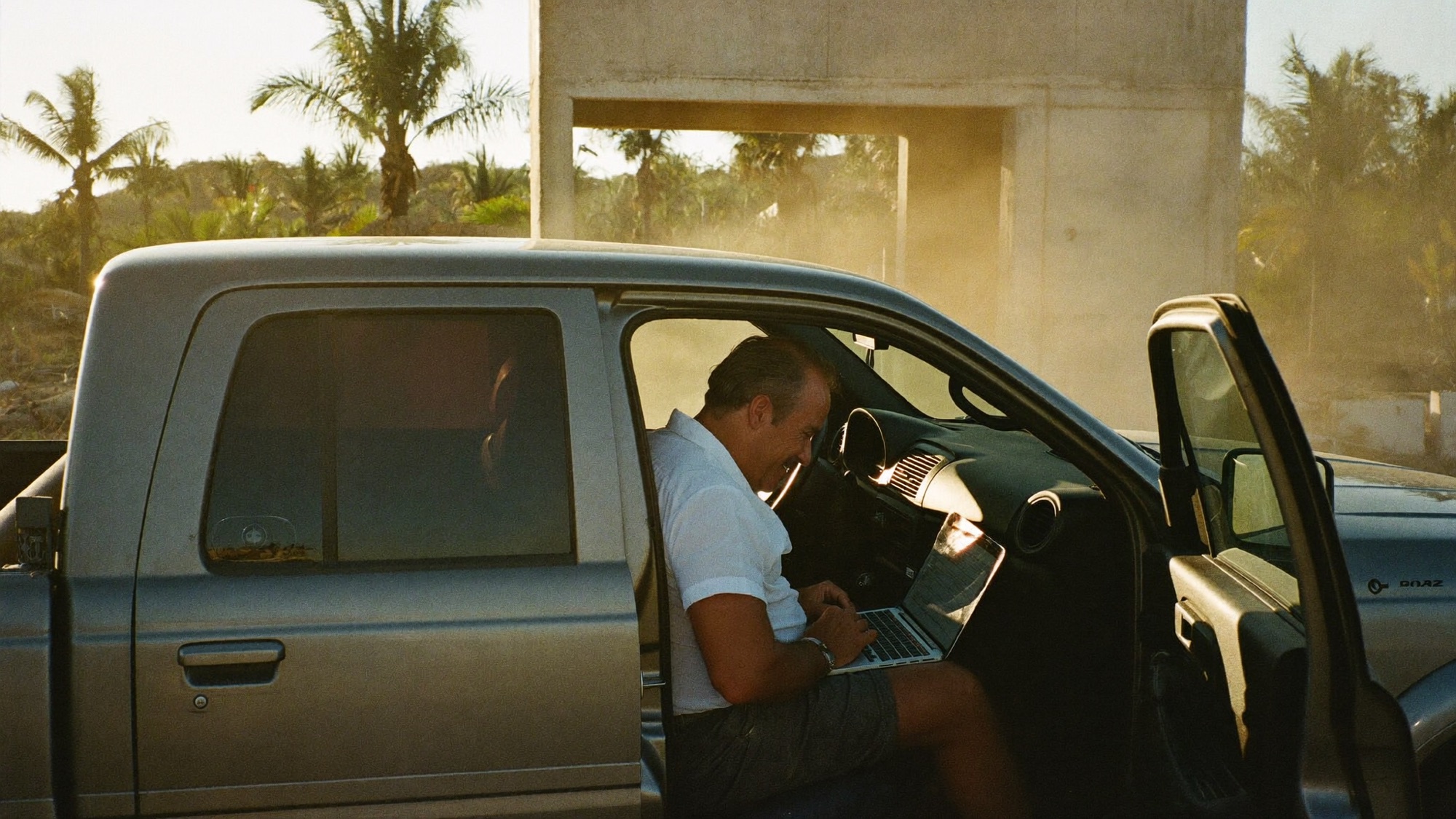 Director de constructora revisando sus obras desde una laptop, sentado en su camioneta al atardecer.